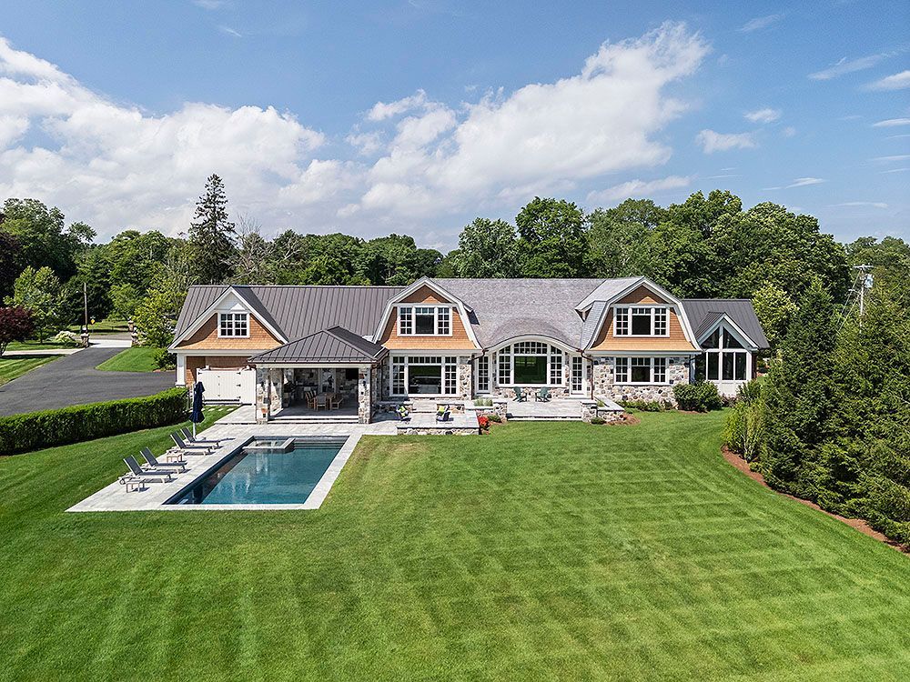 Large house with a pool, green lawn, and trees under a blue sky.