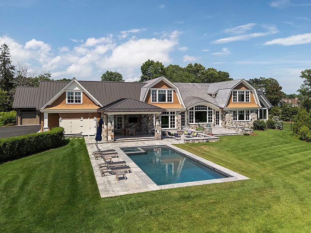 House with pool; stone and wood exterior, garage on the left, sunny day.