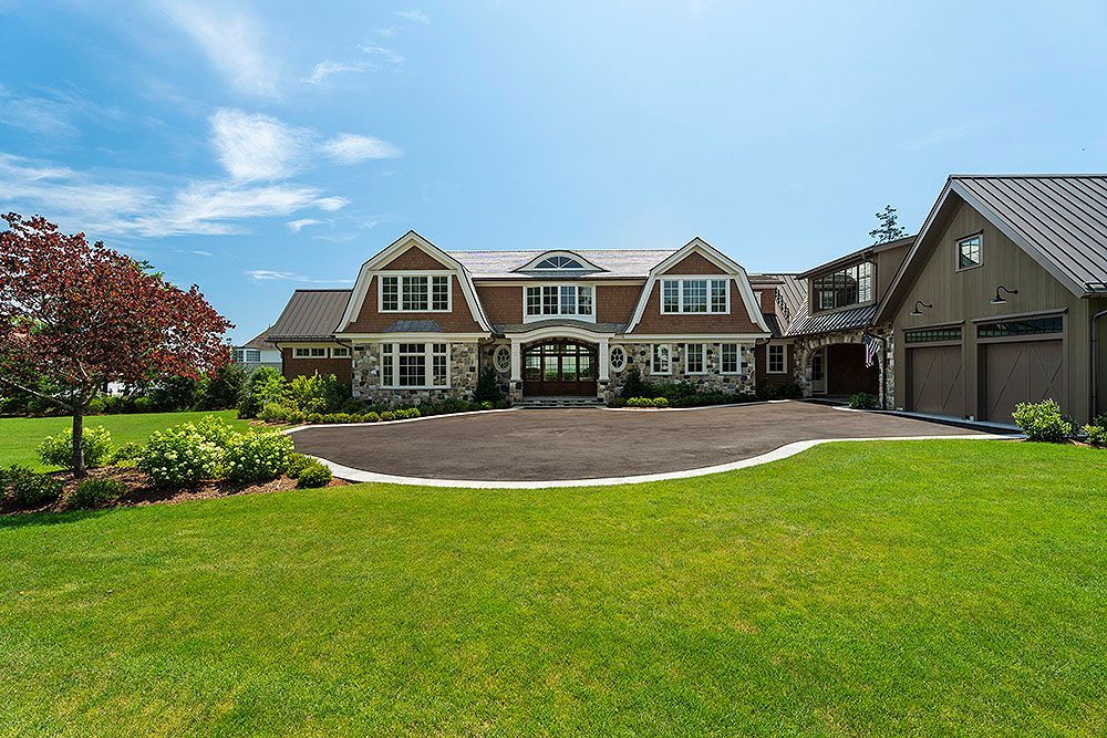 Large, brown and stone home with green lawn, blue sky and detached garage.