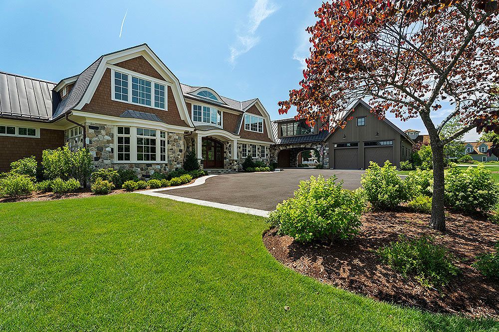Luxurious house with stone and brown siding, driveway, and manicured lawn on a sunny day.