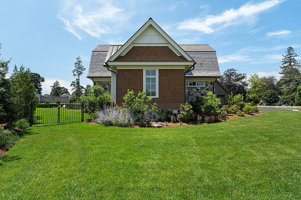 Back view of a brick cottage with a green lawn, blue sky, and trees.