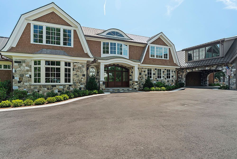 Stone and wood exterior of a large house with a paved driveway and blue sky.