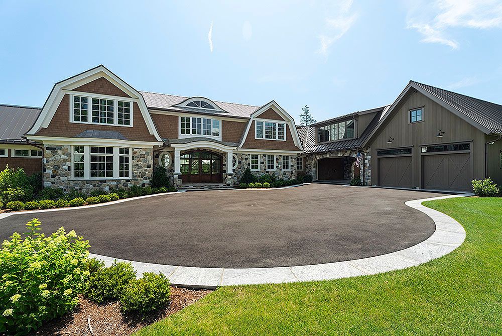 Large brown house with stone accents, circular driveway, and green lawn.