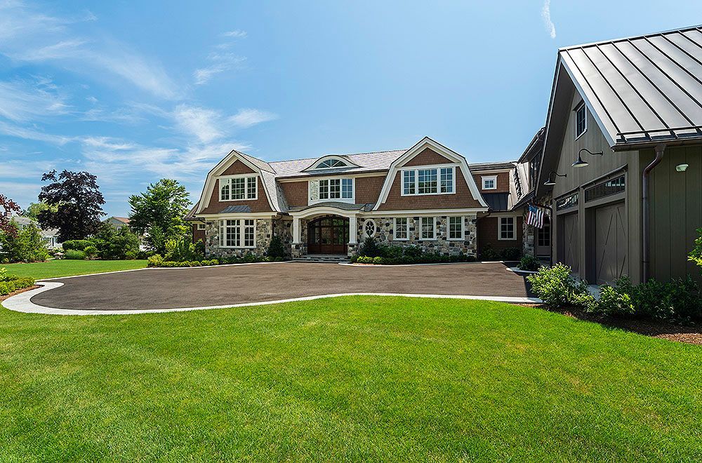 Large house with stone and brown exterior, green lawn, and blue sky.