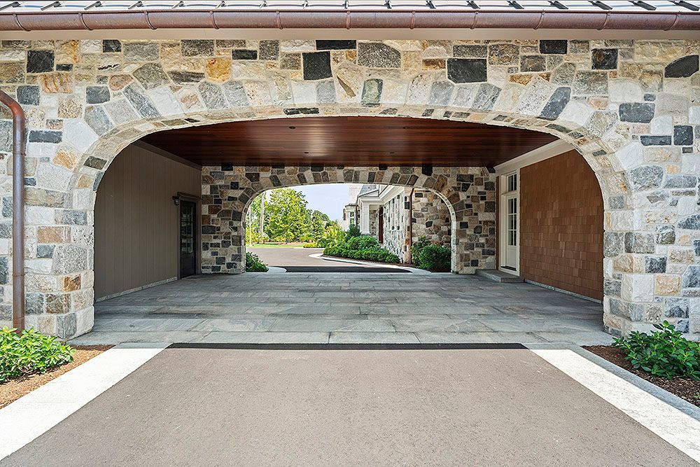 Stone archway over a paved driveway leads to a street with greenery.