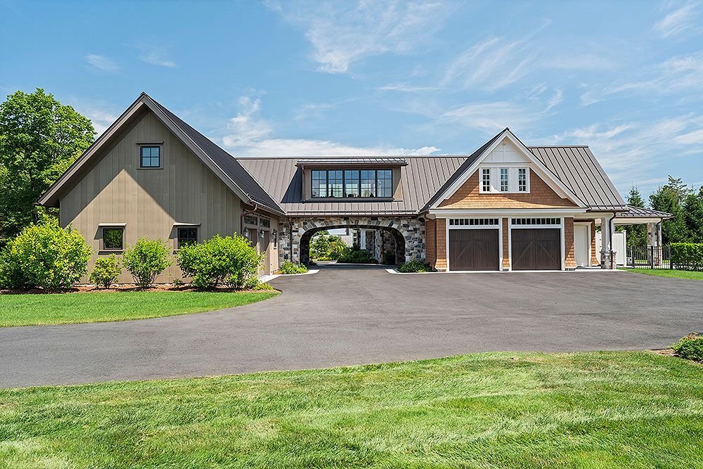 House with brown siding, driveway, garage with brown doors, and green lawn under a blue sky.