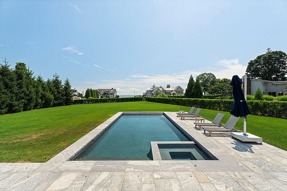Pool with built-in hot tub, chaise lounges, and umbrella on stone patio exterior project