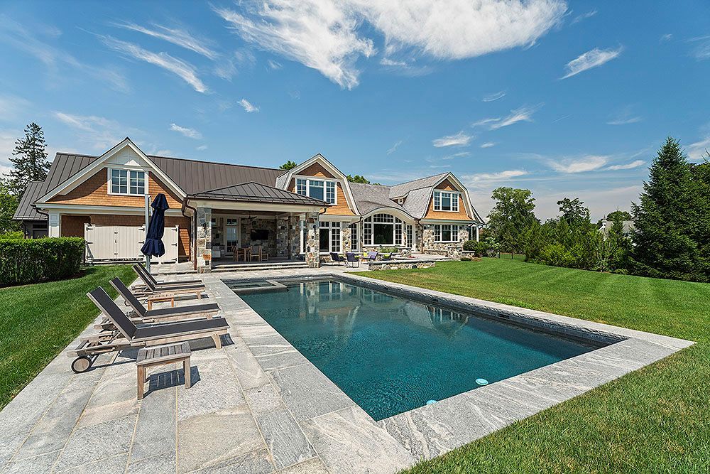 Luxurious house with a pool and lounge chairs on a bright sunny day.