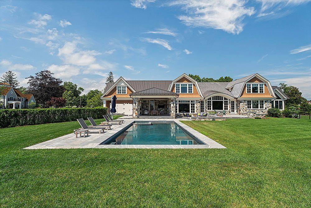 A large, luxurious house with a pool in a grassy backyard under a blue sky.