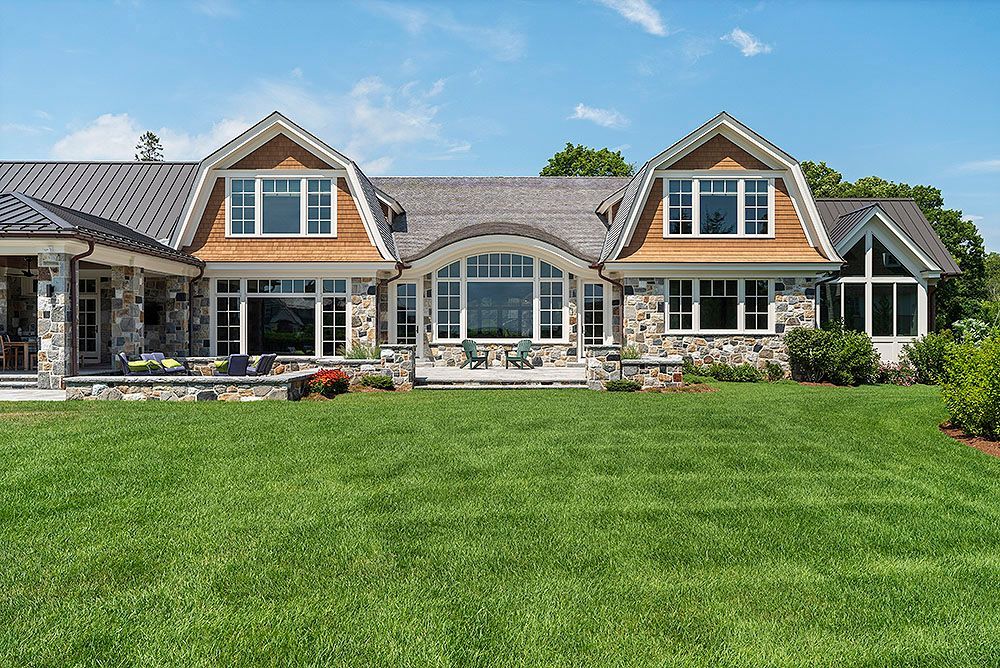 Lush green lawn in front of a large home with stone and wood exterior under a blue sky.