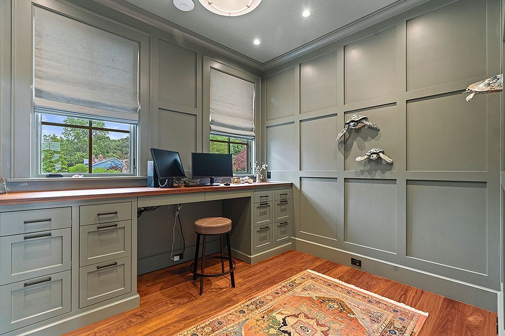 Home office with green paneling, desk with computer, and rug on wooden floor.