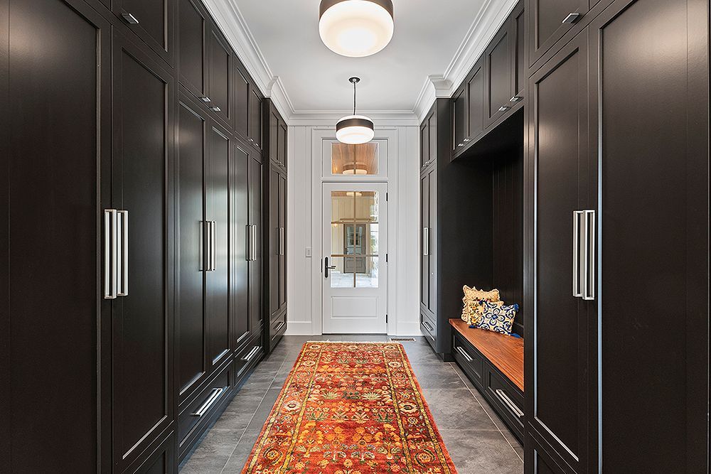 A dark, narrow hallway with built-in black cabinets on either side, a patterned rug, and a doorway at the end.