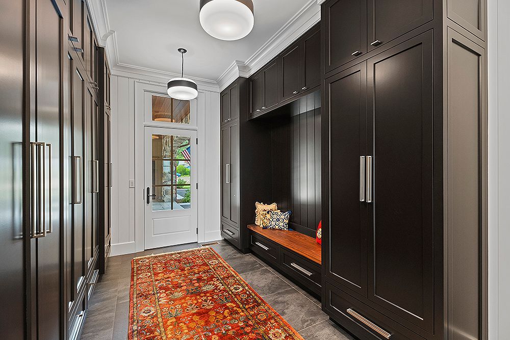 Dark-paneled hallway with bench, rug, and door. Built-in cabinets line the walls, with a light fixture overhead.