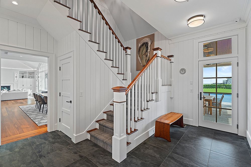 Entryway with stairs, bench, and door to patio. White walls, dark floor, and natural wood accents.