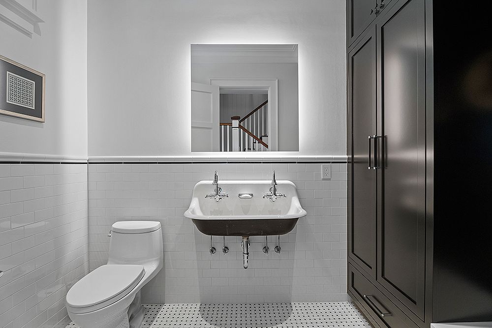 A modern bathroom with white tile, toilet, sink, and dark cabinet. A mirror is centered above the sink.