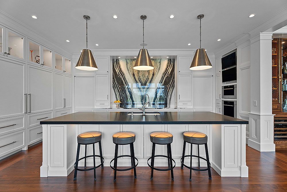 Modern white kitchen with black island countertop, pendant lights, and four stools.