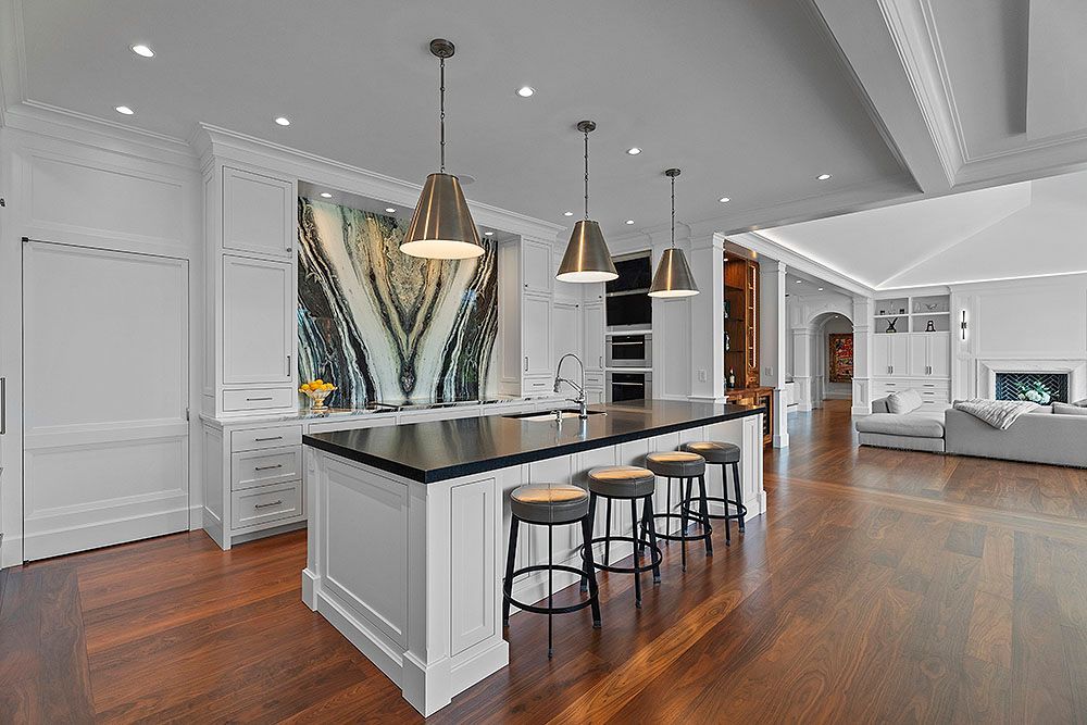 Elegant kitchen with dark wood floors, white cabinetry, island with stools, and abstract art backsplash.
