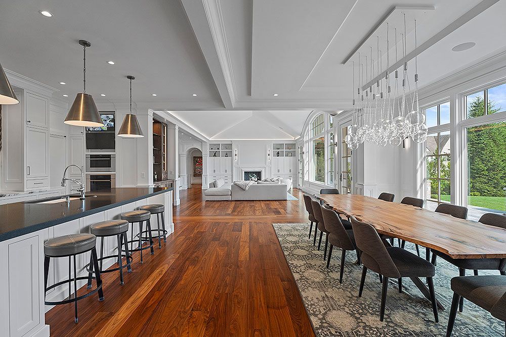 Open-concept kitchen/dining room with island seating, long table, hardwood floors, and tall windows.
