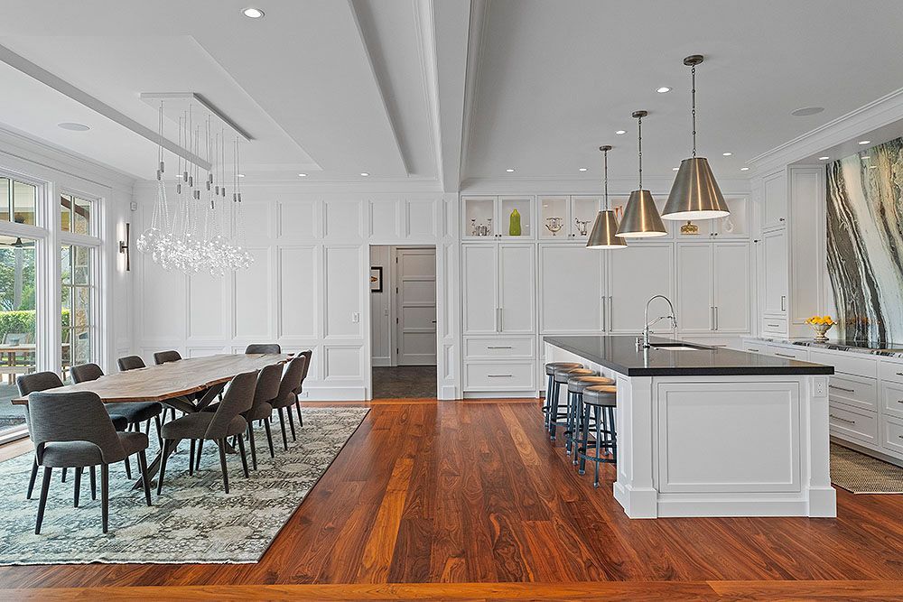 Spacious white kitchen and dining area with wooden floors, large island, and elegant light fixtures.