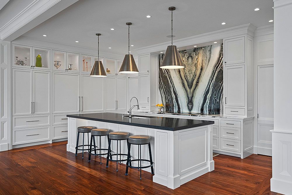 Elegant white kitchen with a black island, wooden floor, and three pendant lights.
