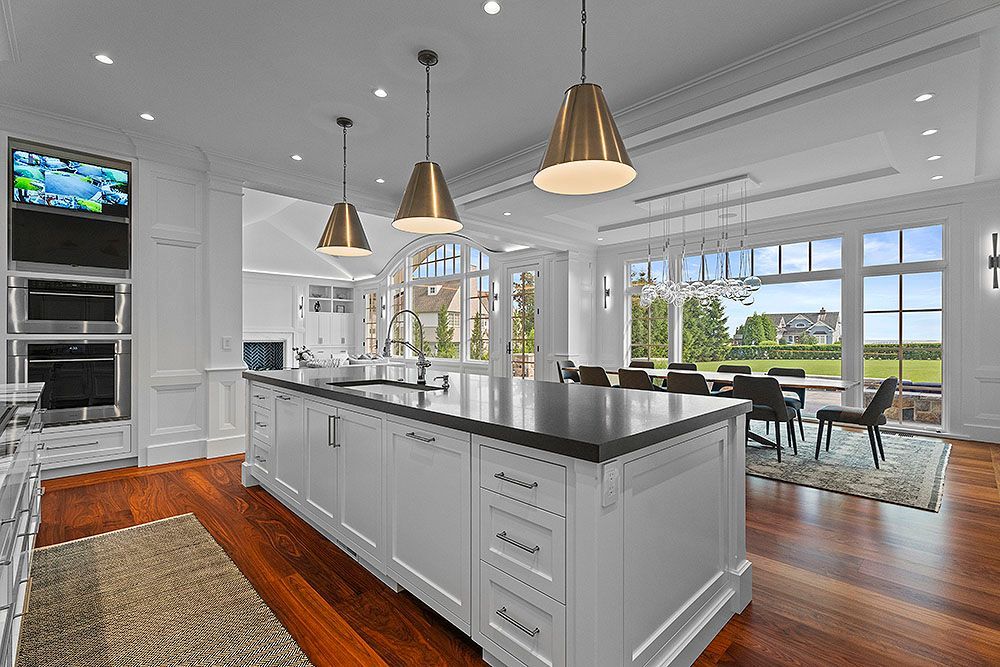Bright white kitchen with island and gold pendant lights, hardwood floors, and a dining area overlooking a green landscape.