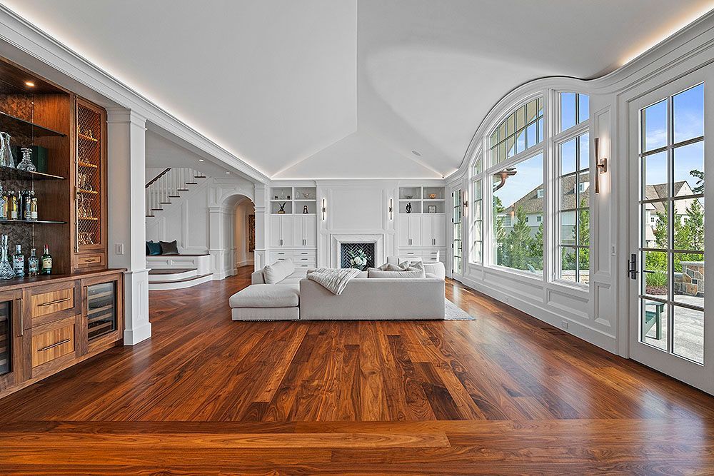 Spacious white-walled living room with wood floors, built-in bar, large windows, and a white couch.