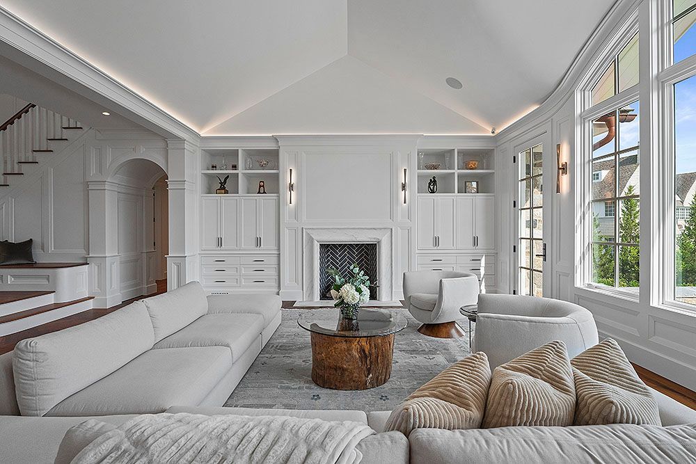 Bright white living room with sectional sofa, fireplace, and large windows.