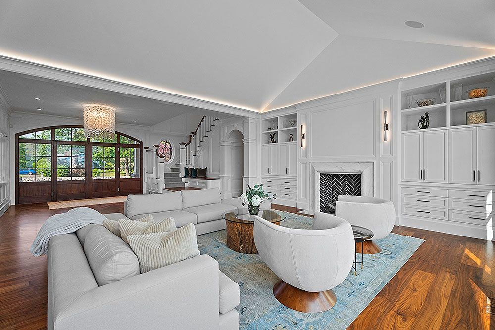 Bright, white living room with a sofa, chairs, fireplace, and built-in shelves. Large arched doorway leads outside.