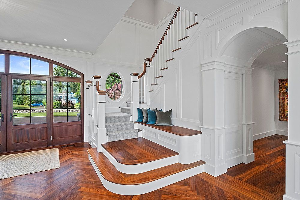 Elegant foyer with a curved staircase, wood floors, and a large arched door.