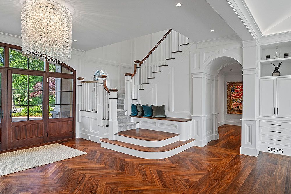 Elegant entryway with wooden floors, staircase, and a large chandelier.