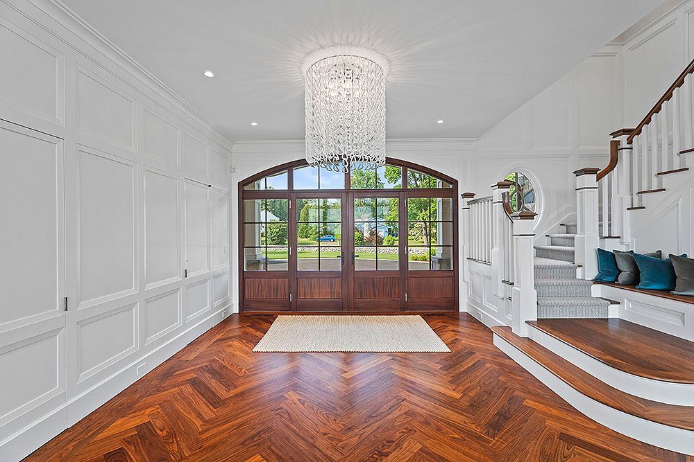 Elegant entry hall with wood floor, staircase, and large glass doors.