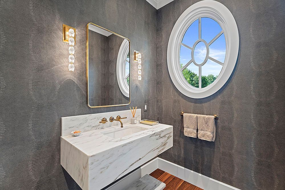 Luxury powder room with marble vanity, oval window, and gold fixtures.