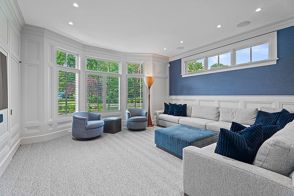 Spacious living room with large windows, blue accent wall, white trim, light gray floors, and blue and gray furniture.