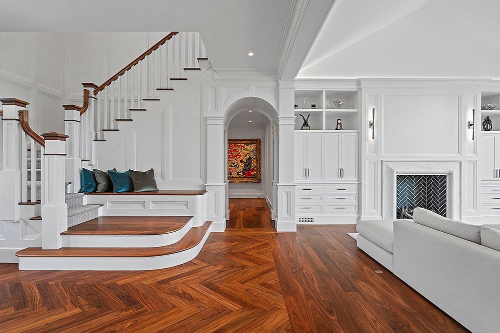 Elegant white interior with wooden floors, staircase, fireplace, and a colorful painting.