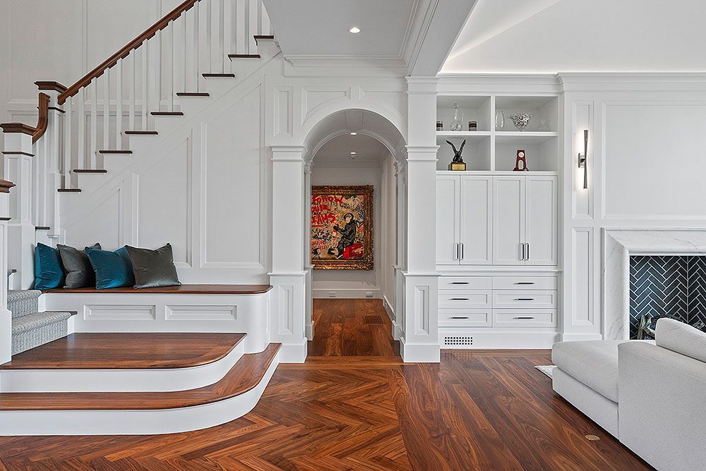 Elegant white-paneled foyer with staircase, built-ins, and arched doorway to a hallway with artwork.