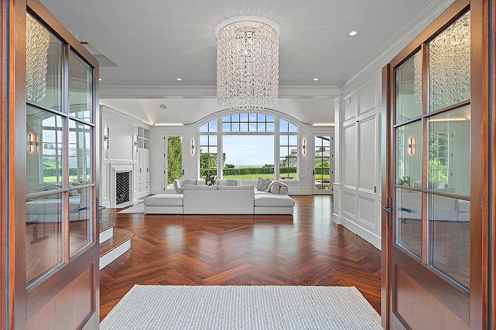 Luxurious home interior with open doors, hardwood floors, and a large window overlooking a lawn.