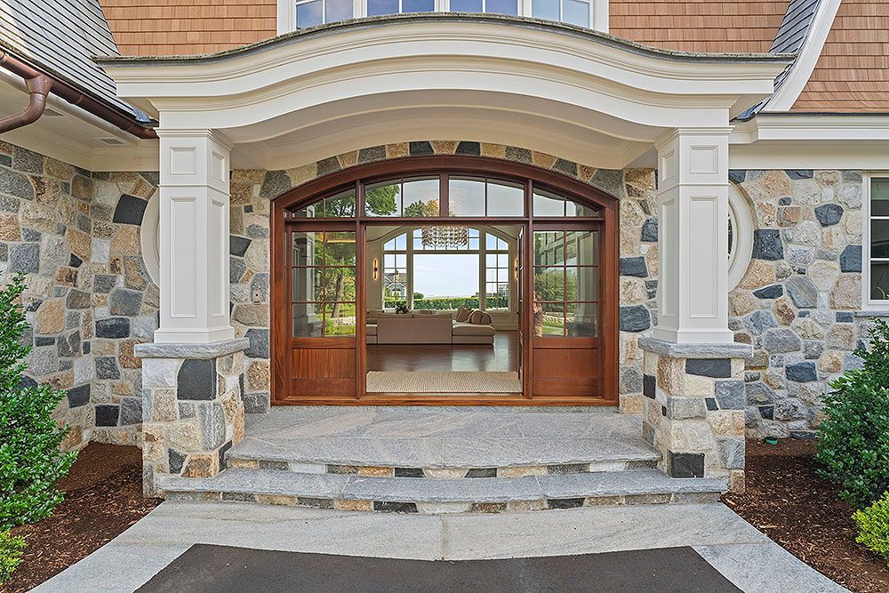 Stone facade entrance with arched wooden doors, steps, and white columns.