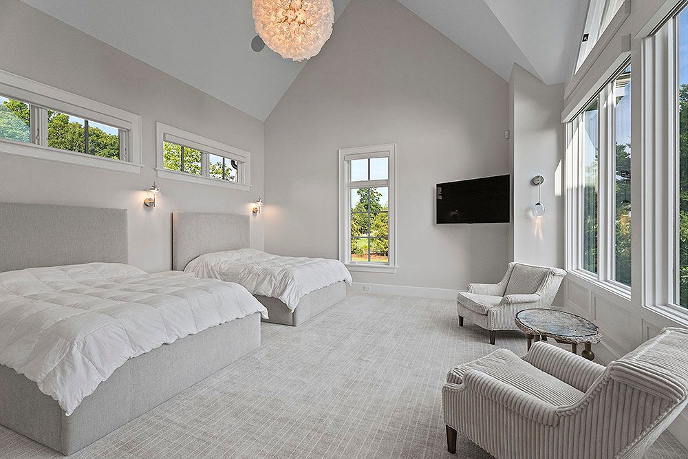 Spacious white bedroom with two beds, sitting area, large windows, and a chandelier.