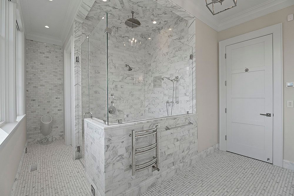 Spacious marble bathroom with glass shower, heated towel rack, and white door.
