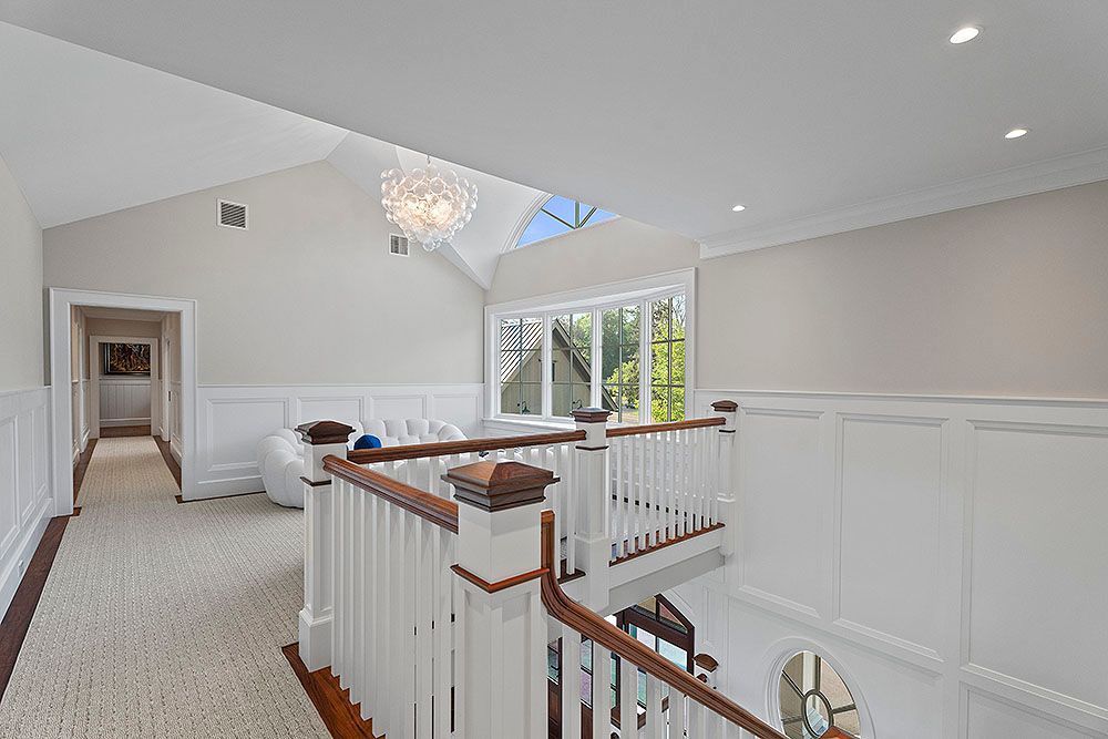 Hallway with white paneled walls, stairs, skylight, chandelier, and neutral carpet.
