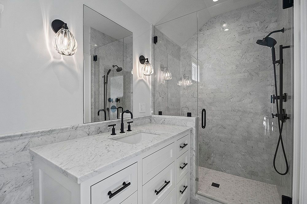 Modern bathroom with white cabinets, marble countertop, glass shower, and black fixtures.