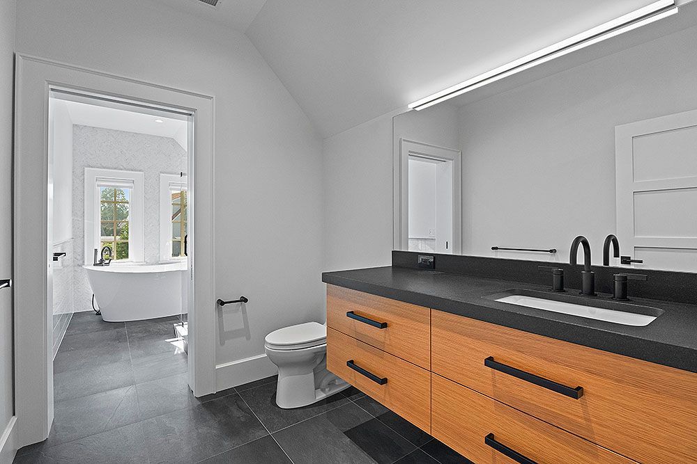 Modern bathroom with wood vanity, black countertop, and access to a separate room with a bathtub.