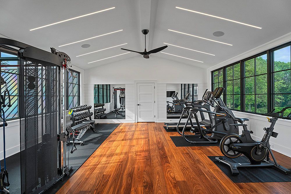 Home gym with wooden floor, exercise equipment, and large windows.