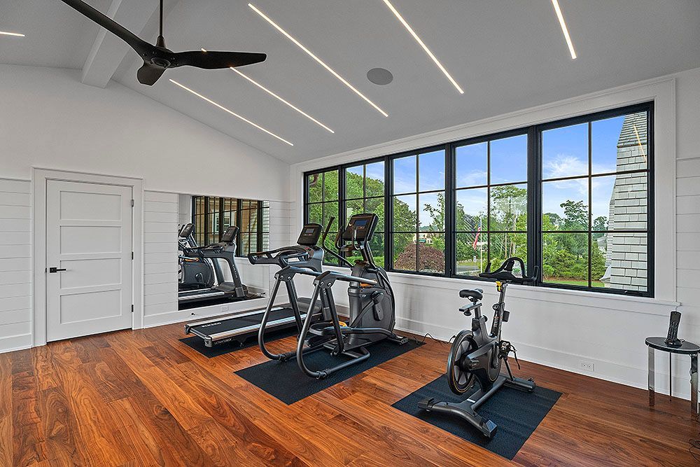 A modern home gym with cardio equipment, a large window, and hardwood floors.