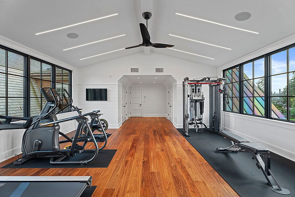 Modern home gym with wood floor, exercise equipment, and large windows.