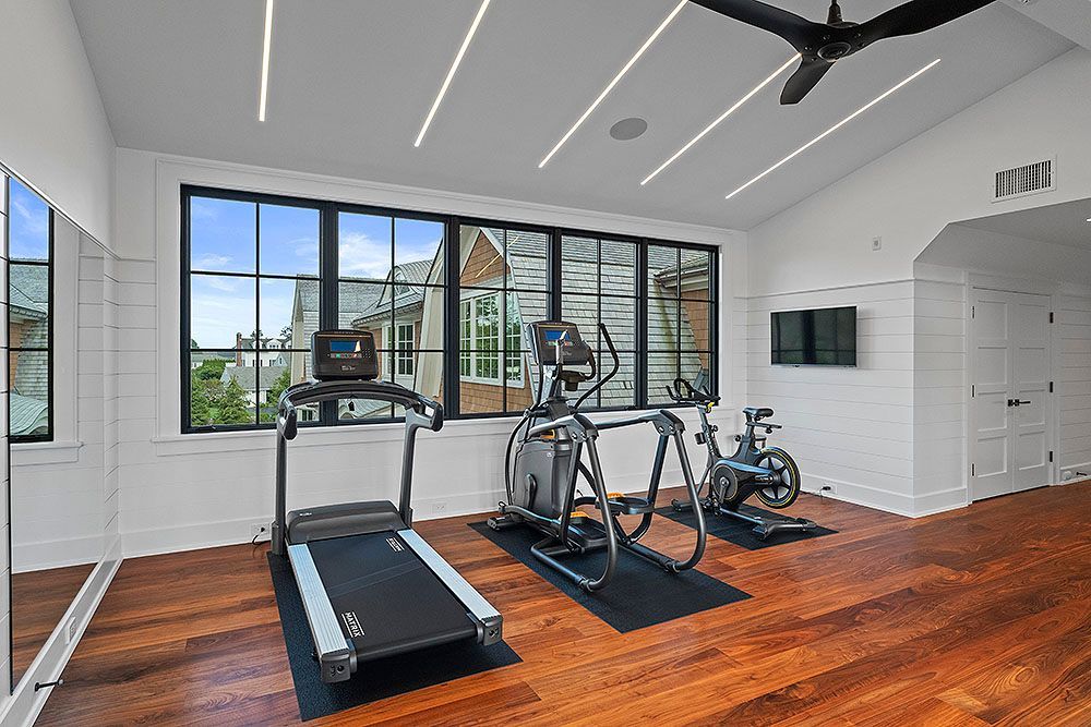 Home gym with treadmill, elliptical, and stationary bike; large windows with outside view.