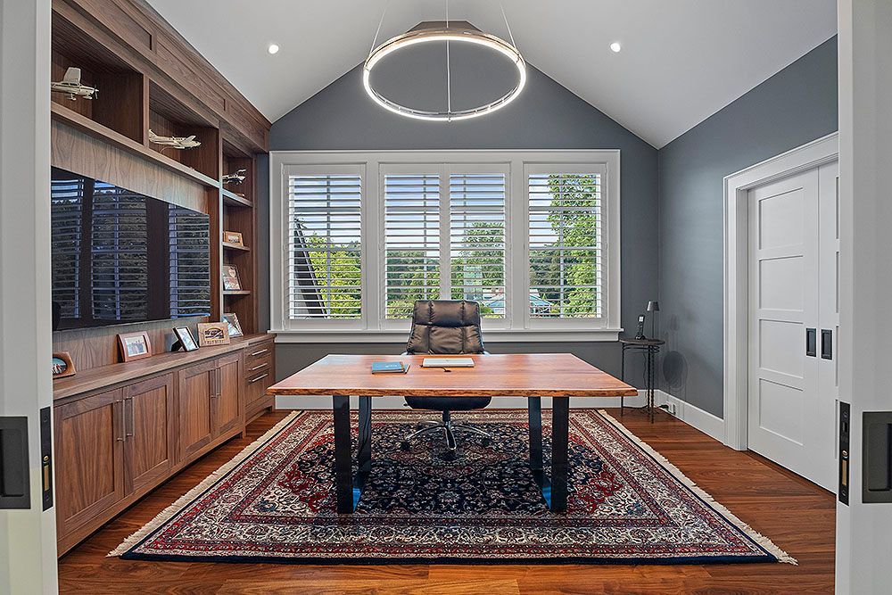 Home office with wooden desk, built-in shelving, and a patterned rug.