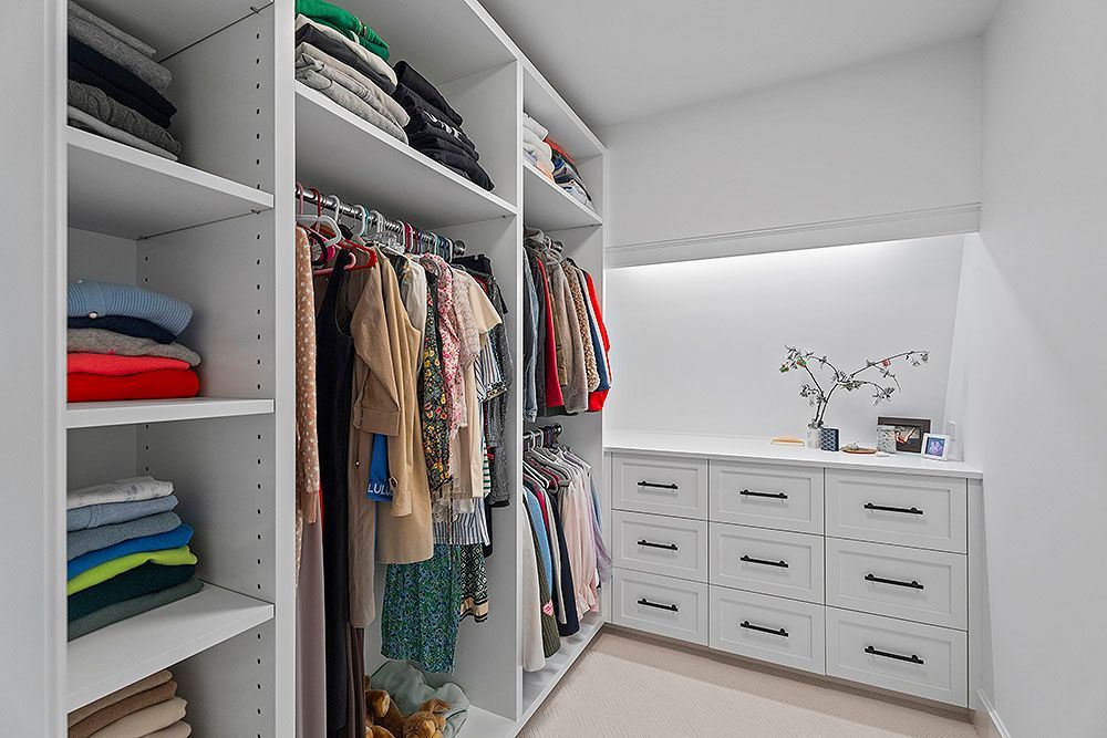 White walk-in closet with shelves, hanging rods, and drawers filled with folded clothes and garments.
