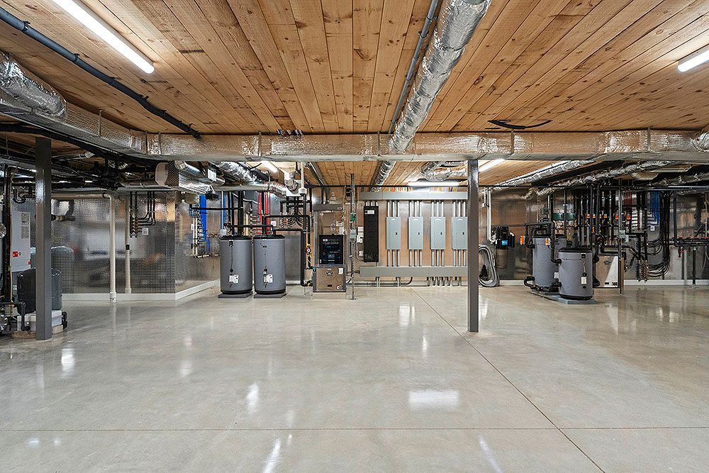Basement with exposed ductwork, pipes, and mechanical systems. Concrete floor, wood ceiling.
