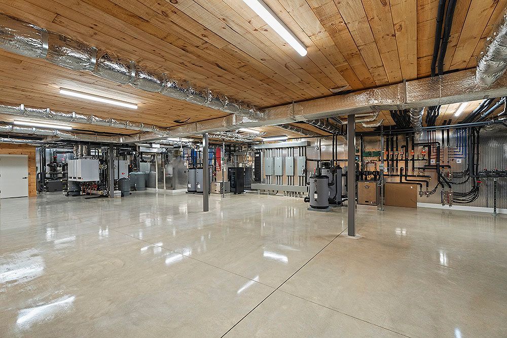 Large industrial-style basement with exposed beams, ductwork, and equipment on polished concrete floor.